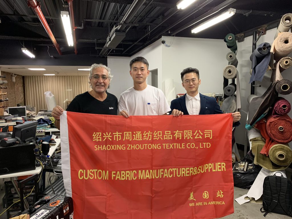 FabricsMaker team with a customer holding a Shaoxing Zhoutong Textile Co. banner in the US